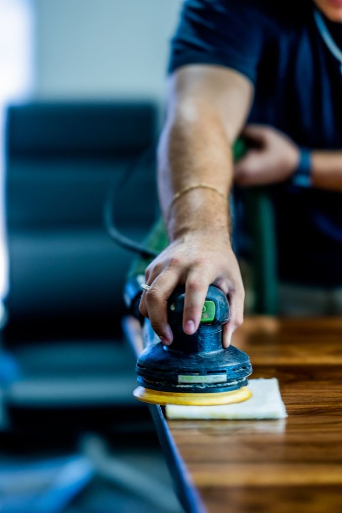 A close-up of a mans hand using a buffing machine on a wooden table indoors.