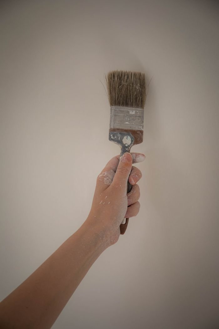 A hand holding a paintbrush, painting a white wall, perfect for home improvement concepts.